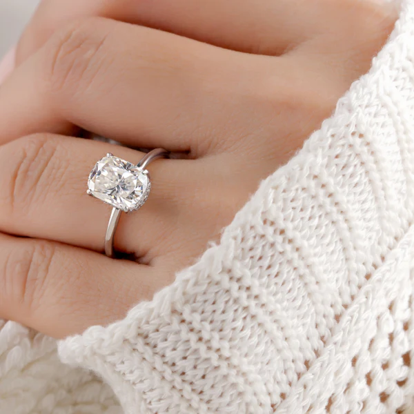 woman's hand extending out of white sweater sleeve with diamond engagement ring on finger